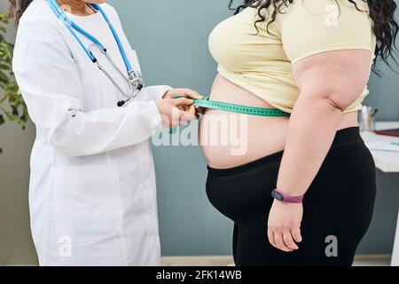 Fettleibigkeit, ungesundes Gewicht. Ernährungsberaterin inspiziert die Taille einer Frau mit einem Meter-Band, um eine Gewichtsabnahme Diät zu verschreiben Stockfoto