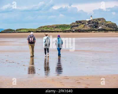 Drei Personen, die im Sommer bei Sonnenschein am Sandstrand von Yellowcraig mit Blick auf Fidra Island und den Leuchtturm, East Lothian, Schottland, Großbritannien, spazieren gehen Stockfoto