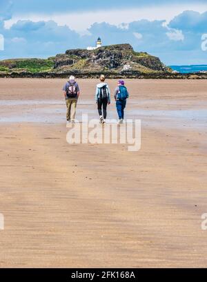 Drei Personen, die im Sommer bei Sonnenschein am Sandstrand von Yellowcraig mit Blick auf Fidra Island und den Leuchtturm, East Lothian, Schottland, Großbritannien, spazieren gehen Stockfoto