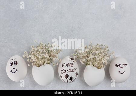 Osterkomposition. Weiße Eier mit lustigen Gesichtern auf dem Tisch. Ein kleines Bouquet in einem Ei. Das Minimalkonzept von Ostern. Eine Osterkarte mit einem Stockfoto