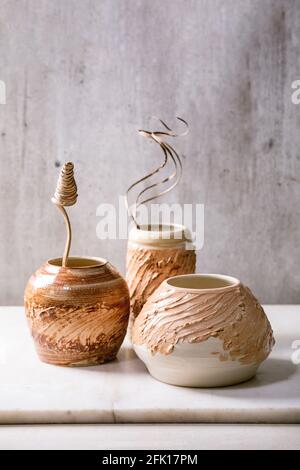 Drei verschiedene Formen beige braune Keramikvasen mit trockenen Blumen und Zweigen verzweigen sich auf einem weißen Marmortisch mit grauer Wand dahinter. Speicherplatz kopieren. Stockfoto