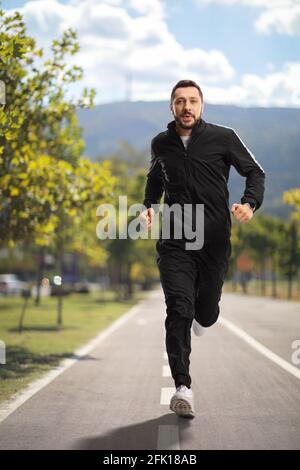 Porträt eines jungen Mannes in schwarzen Trainingsanzügen Laufen auf einer Joggingstrecke Stockfoto