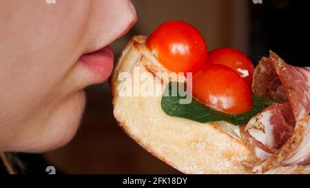 Nahaufnahme. Frau beißt frische Bruschetta mit Kirschtomate Stockfoto
