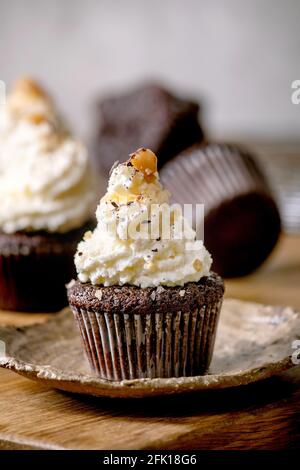 Hausgemachte Schokoladen-Cupcakes Muffins mit weißer Buttercreme und gesalzenem Karamell auf Keramikplatte auf Holztisch. Stockfoto