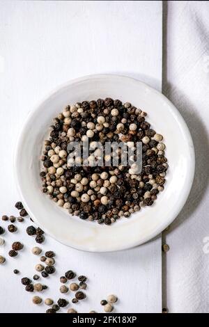 Mischung aus schwarzen und weißen Pfefferkörnern würzige Pfeffer Gewürze in weißem Teller auf Holzbrett. Weißes Tuch als Hintergrund. Flach liegend, Platz Stockfoto