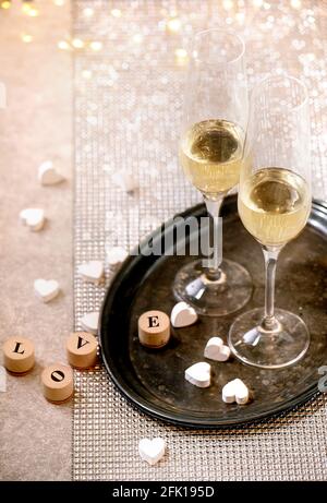 St. Valentine oder Hochzeit Grußkarte mit zwei Champagner Gläser auf Tablett stehen auf silbernen funkelnden Tisch, weiße Herzen, Bokeh Lichter. Liebe Schreibschrift Stockfoto