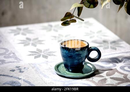 Tasse türkischer schwarzer Schaumkaffee auf einem kunstvollen Keramiktisch mit Eukalyptuszweigen. Sonnenlicht Stockfoto