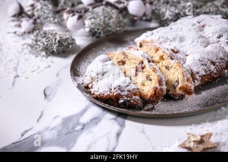 Traditionelle hausgemachte deutsche Weihnachten backen Stollenkuchen Brot auf Teller mit silbernen Weihnachtsdekorationen auf weißem Marmor Hintergrund. Stockfoto
