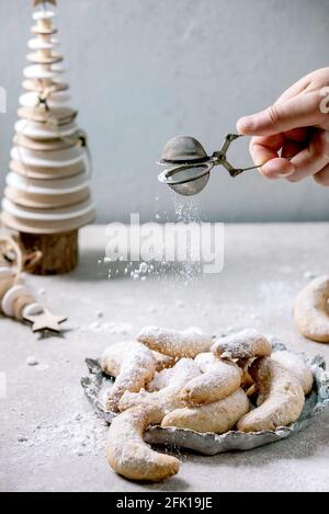 Hausgemachte traditionelle Weihnachten Mürbeteig Cookies Vanille Crescents mit Puderzucker bestreuen aus Sieb. Auf Keramikplatte mit hölzernen Weihnachtsdecorati Stockfoto