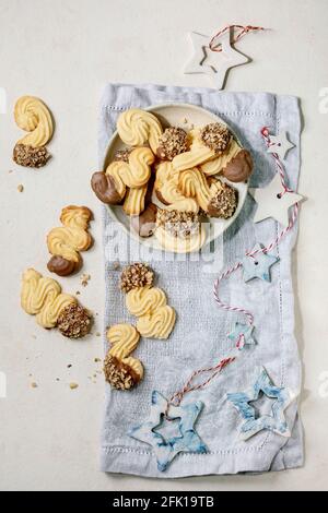 Hausgemachte traditionelle Mürbeteig-Cookies in verschiedenen Formen mit Schokolade Glasur und Nüsse. Auf Keramikplatte mit Weihnachtssternen Dekorationen über weißem Hintergrund Stockfoto