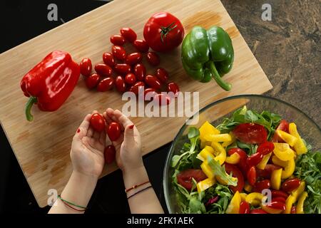 Nahaufnahme von Kinderhände, Kind wird mit Tomaten gespielt und bereitet einen Salat aus Gemüse und Kräutern. Draufsicht. Stockfoto