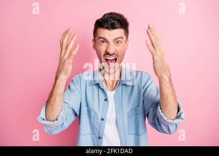 Foto eines wütenden jungen Mannes, der die Hände aufhebt und laut schreit Verärgert isolieren pastellrosa Farbe Hintergrund Stockfoto