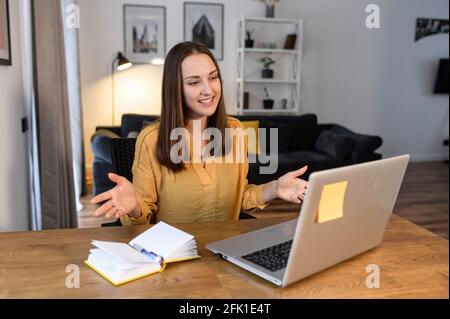 Eine junge Frau, die im Heimbüro einen Laptop für Videokonferenzen nutzt. Eine intelligente Frau in schaut auf Webcam und spricht mit einem Lächeln. Fernkommunikationskonzept Stockfoto