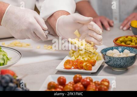 Chefkoch mit Handschuhen, der mit seinem Messer geschnittene Äpfel auf ein Gericht legte: Selektiver Fokus Stockfoto