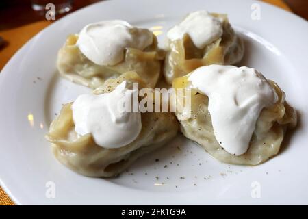 Manty mit Pfeffer und saurer Creme auf dem Teller im Restaurant Stockfoto