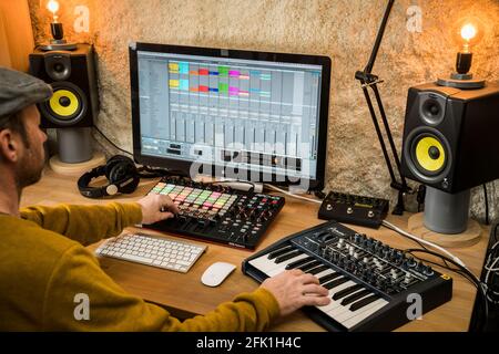 Elektronischer Musiker in einem Heimstudio. Arbeiten mit einem Midi-Controller, einem Synthesizer und Ableton Live DAW auf einem Mac-Computer Stockfoto