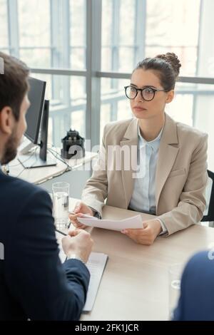 Seriöse junge Frau mit Haarsträhne am Tisch sitzen und Analyse des Vertrags mit einem Rechtsanwalt im Amt Stockfoto