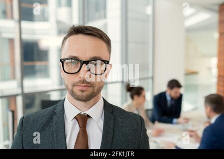 Porträt eines seriös aussehenden Rechtsmediziners mit Stoppeln, die dagegen stehen Kollegen diskutieren die Tagesordnung im Hintergrund Stockfoto