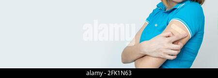 Nicht erkennbare Frau in einem blauen T-Shirt und einer Brille mit einem Pflaster auf der Hand freut sich über eine Impfung gegen Coronavirus-Infektion Covi Stockfoto