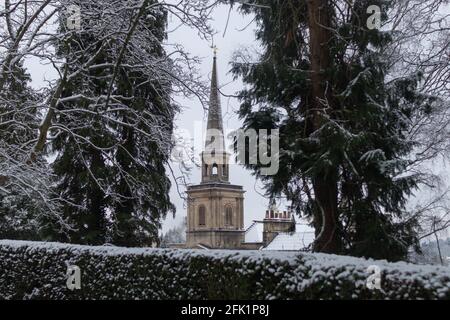 Ein schneebedeckter Kirchturm, umgeben von Bäumen auf Schnee Tag in England Stockfoto