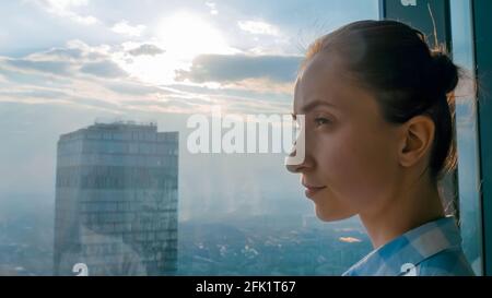 Frau, die das Stadtbild durch das Fenster des Wolkenkratzers - Seite betrachtet Anzeigen Stockfoto