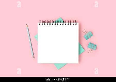 Arbeitsbereich mit offenem Notizblock-Modell und Minzpapier auf rosa Hintergrund. Layout der Schule. Stockfoto