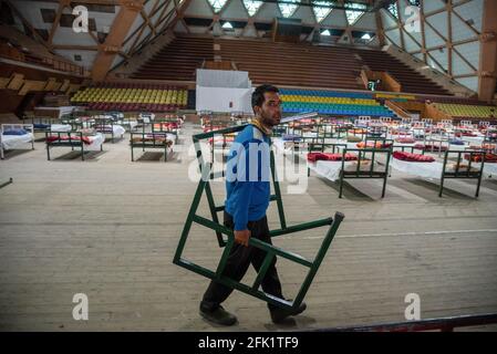 Srinagar, Indien. April 2021. Ein Arbeiter trägt Teile eines Bettes, das für das Covid-19 Isolationszentrum in einem Hallensportstadion in Srinagar eingerichtet werden soll. Die Jammu und Kaschmir meldeten 3,164 positive Fälle, die höchsten seit dem Ausbruch der Covid-19-Pandemie im vergangenen Jahr, was die Zahl der aktiven Fälle auf 22,283 anschob, die sonst etwa einen Monat zuvor weniger als 600 waren. Eine 20-jährige Frau wurde unter den fünfundzwanzig Todesfällen in J&K in den letzten 24 Stunden gemeldet, was die Todesrate auf 2,197 betrug. Kredit: SOPA Images Limited/Alamy Live Nachrichten Stockfoto