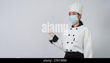 Koch trägt Gesichtsschutzmaske oder Atemschutzmaske zum Schutz vor Viruserkrankungen. Lebensmittelsicherheit und Coronavirus-Pandemie. Chef posiert Geste r Stockfoto