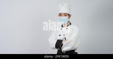 Koch trägt Gesichtsschutzmaske oder Atemschutzmaske zum Schutz vor Viruserkrankungen. Lebensmittelsicherheit und Coronavirus-Pandemie. Chef posiert Geste r Stockfoto