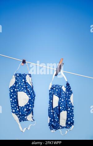 Zwei handgemachte, wiederverwendbare, waschbare Stoffmasken, die an der Wäscheleine gegen den blauen Himmel hängen. Konzept der Umweltfreundlichkeit, Hygiene Stockfoto