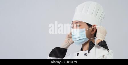 Koch trägt Gesichtsschutzmaske oder Atemschutzmaske zum Schutz vor Viruserkrankungen. Lebensmittelsicherheit und Coronavirus-Pandemie. Chef posiert Geste r Stockfoto