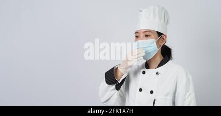 Koch trägt Gesichtsschutzmaske oder Atemschutzmaske zum Schutz vor Viruserkrankungen. Lebensmittelsicherheit und Coronavirus-Pandemie. Chef posiert Geste r Stockfoto