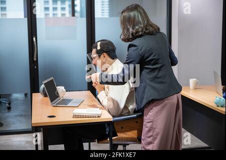Asiatische Geschäftsfrau Beratung mit glücklich und lächelnd Homosexuell Kollegen tragen Gesichtsschutz am Schreibtisch im modernen Büro Stockfoto