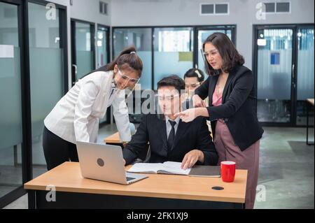 Glückliche asiatische Managerin, die sich mit Kollegen berät und zusammenarbeitet Mit Laptop am Schreibtisch im Büro Stockfoto