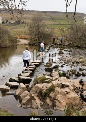 Wanderer überqueren die Trittsteine über den Fluss Doe, Ingleton, Yorkshire Dales National Park, Großbritannien Stockfoto