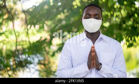 Afrikanischer Mann mit Gesichtsmaske betet im Glauben gegen Corona Virus oder COVID-19.16:9 Stockfoto