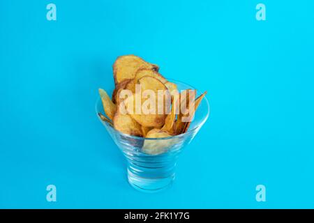 Frisch gebackene hausgemachte Kartoffelchips in einer Glasschüssel mit lebhaftem Hintergrund. Stockfoto