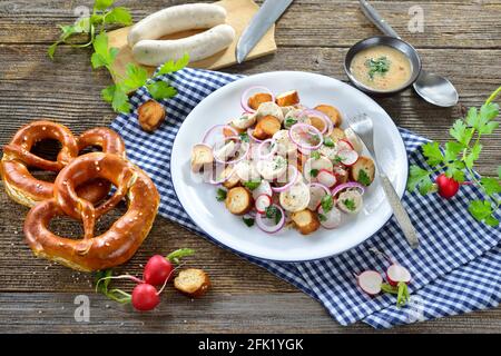 Herzhafter bayerischer Salat mit geschnittenen Kalbswürsten, gebratenen Brezelscheiben und einem Senfdressing auf einem rustikalen Holztisch Stockfoto