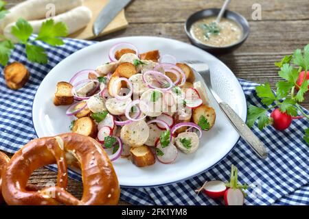 Herzhafter bayerischer Salat mit geschnittenen Kalbswürsten, gebratenen Brezelscheiben und einem Senfdressing auf einem rustikalen Holztisch Stockfoto