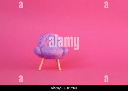 Ein Miniatur-Stuhl aus Filz mit rosa Hintergrund. Nadelverfilzter Miniaturstuhl. Stockfoto