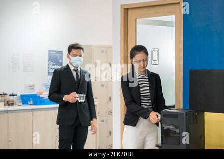 Büroangestellte stehen in der Schlange mit einer Kultur der sozialen Distanzierung Um in der Kaffeepause einen Kaffee aus der Kaffeemaschine zu machen Im Coworking Space Stockfoto