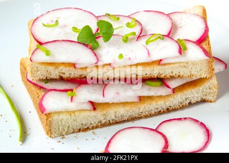 Gerösteter Toast mit frisch gehackten Radieschen und grünen Kräutern auf dem weißen Teller. Gesundes Frühstück. Sandwich mit Gemüse. Nahaufnahme Stockfoto