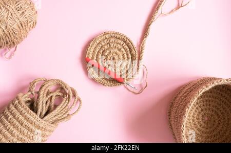 Der gestrickte Teil des Korbes besteht aus Jute-Seil und einem Häkelhaken auf beigem Hintergrund. Hobbys, Handarbeiten, Organisation des Raumes. Stockfoto