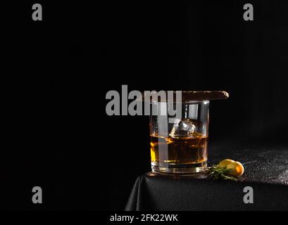 Cognac, Rum, Whiskey oder anderes alkoholisches Getränk in einem Glas auf schwarzem Hintergrund. Zigarre auf einem Glas, Kopierraum. Stockfoto