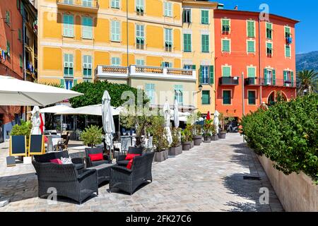 Blick auf die schmale Straße, ein Restaurant im Freien und farbenfrohe Häuser in der Altstadt von Menton, Frankreich. Stockfoto