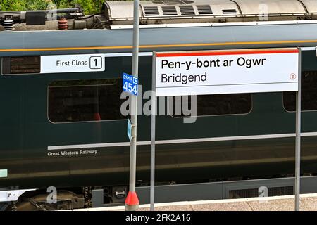 Bridgend, Wales - April 2021: Zweisprachiges Schild mit dem Namen des Bahnhofs in Bridgend. Im Hintergrund ist der erstklassige Wagen eines Zuges zu sehen Stockfoto