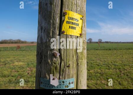 Ländliche Breitbandnetze, die durch ein „Vorsicht-Overhead-Glasfaserschild“ auf der Seite des britischen Suffolk veranschaulicht werden. Stockfoto