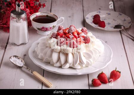 Rote Frucht pavlova mit einer Tasse Tee auf einem Holztisch Stockfoto