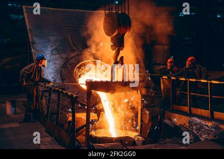 Gießen von hellem flüssigem Eisen oder Metall mit Funken in Behälter in Stahlmühle oder Werkstatt Hochofen Gießerei. Metallgussverfahren in der metallurgischen Fabrik. Stockfoto