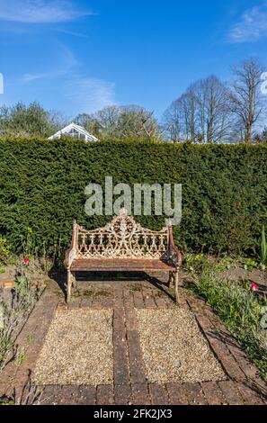 Eine schäbige, schicke, dekorative, rostig weiß lackierte Metallbank im Garten im Dunsborough Park, Ripley, Surrey, Südostengland Stockfoto